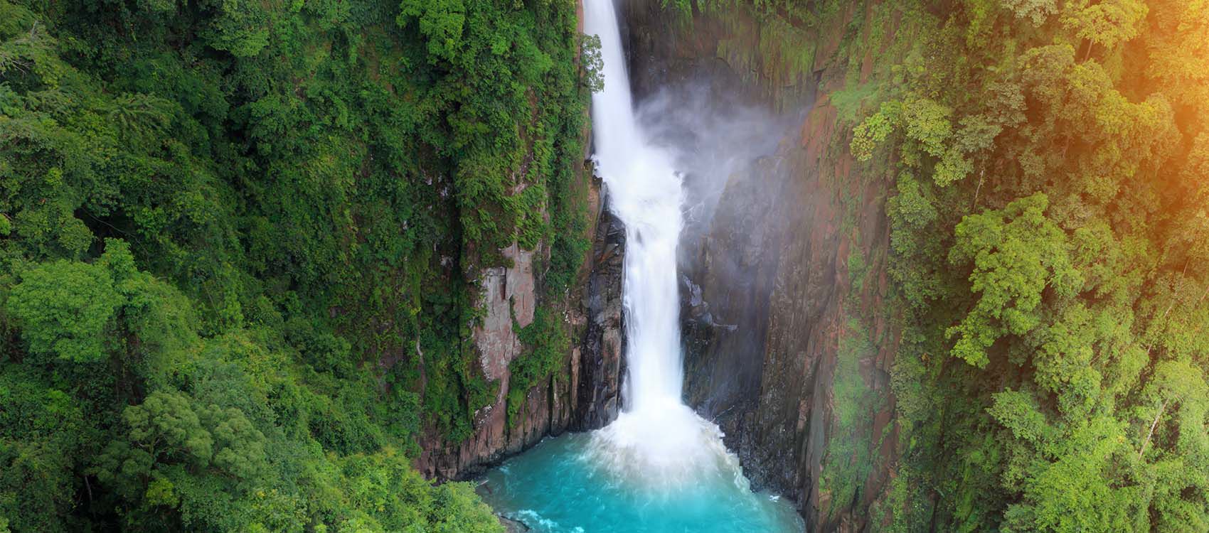 aqua waterfall cuts through tropical forest cliff