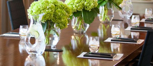boardroom table set with green flowers, water and notepads