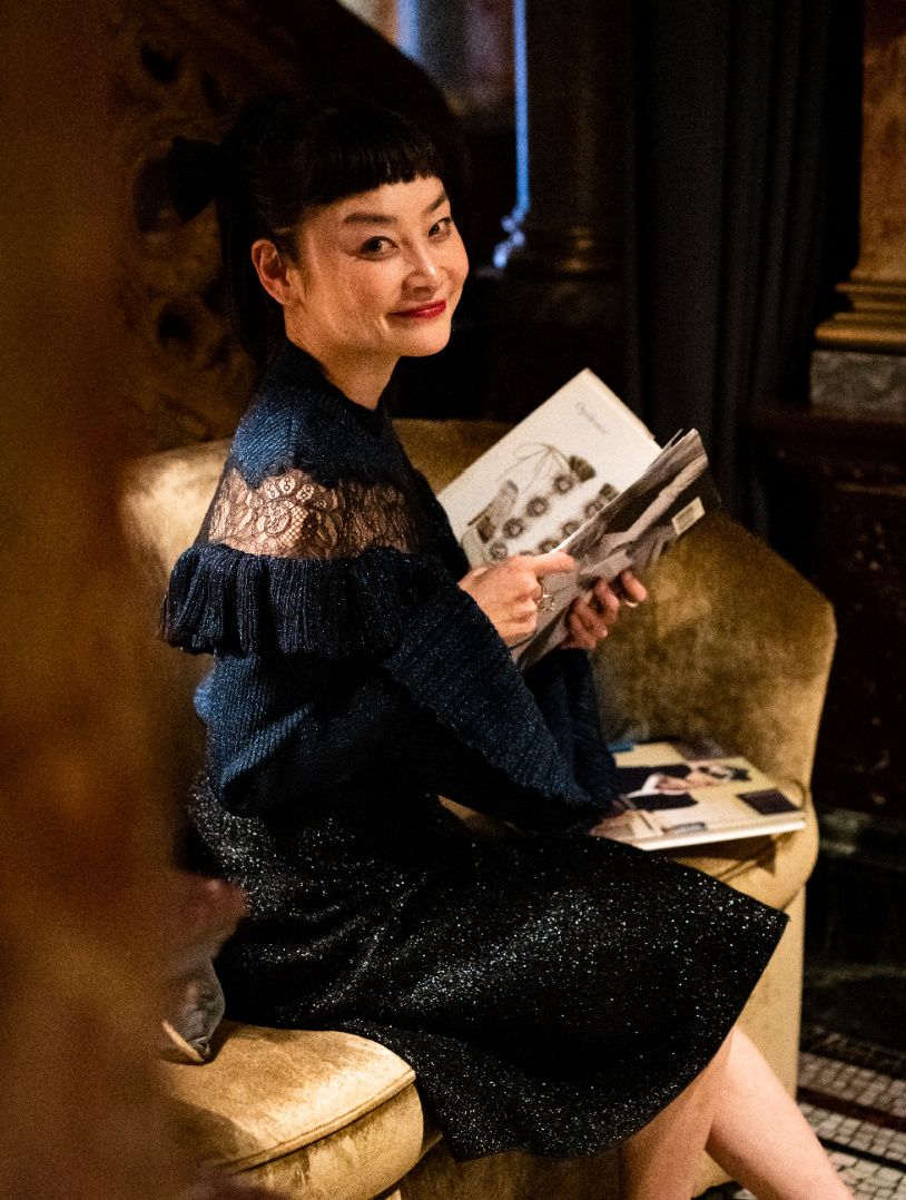 woman dressed up in black sitting on a gold couch looking at books