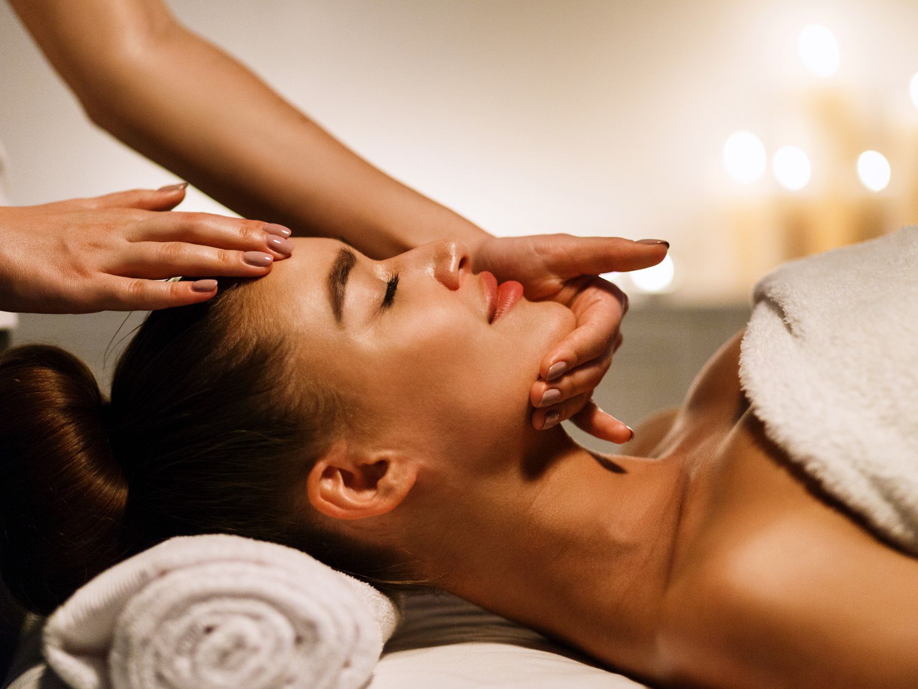 Person receiving a relaxing head and neck massage in a spa setting with soft candlelight.