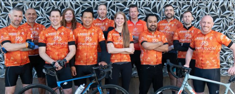 a dozen chefs in cycling gear standing with bicycles