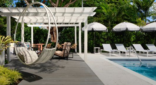 White pergola and circular hanging chair beside pool