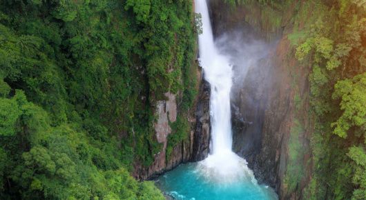 aqua waterfall cuts through tropical forest cliff