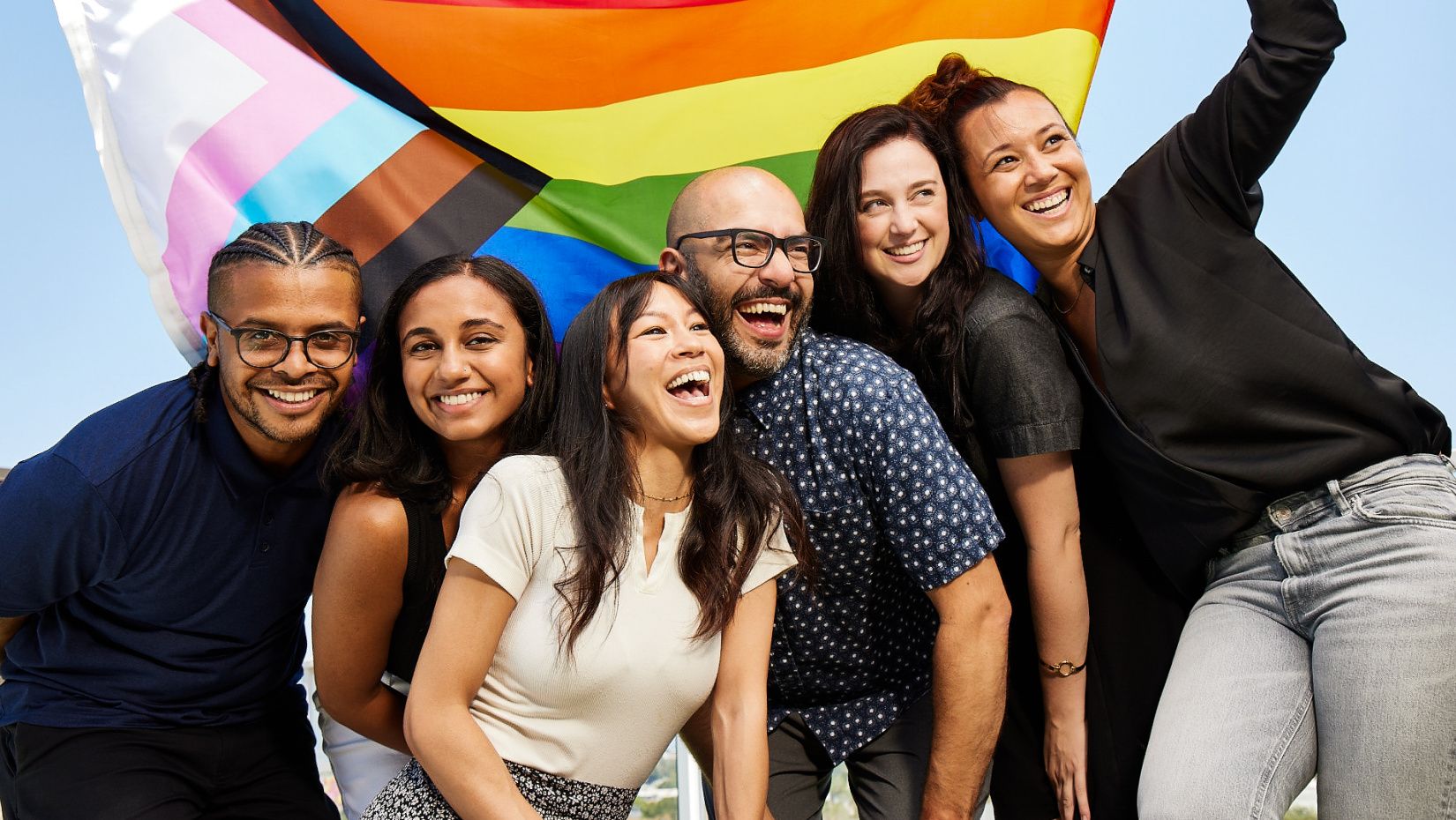 group of people smiling and holding up a rainbow flag