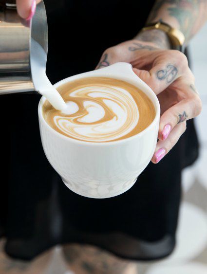 tattooed fingers pouring coffee into white porcelain cup