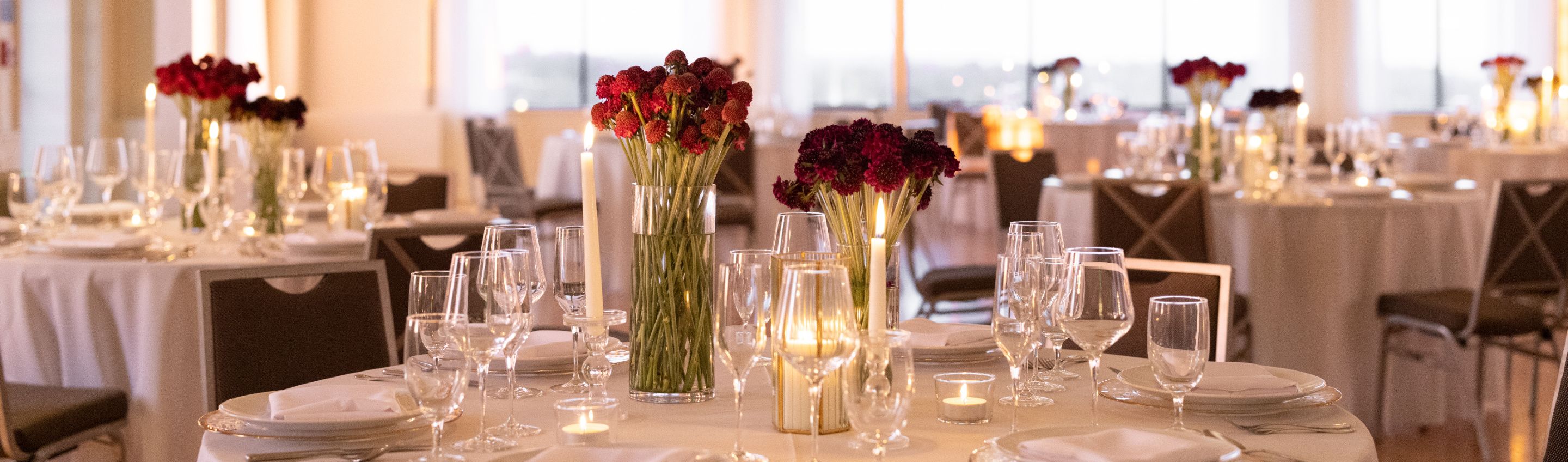 round tables, white tablecloths with stemware and centerpieces with red flowers and candles