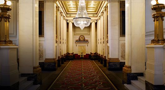 Grand hallway with red carpet, large marble pillars, and crystal chandelier
