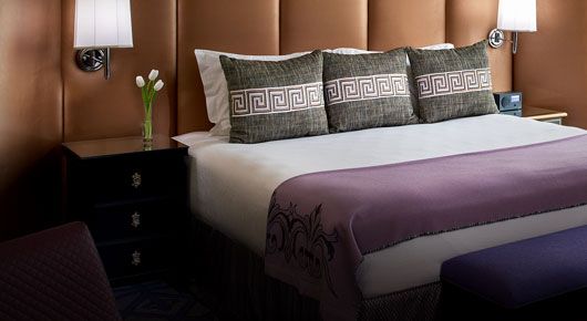 Hotel room with king bed and purple accent blanket and chocolate brown padded backwall