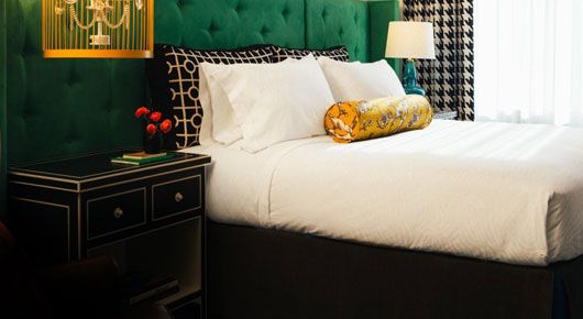 hotel room with bright deep green headboard with black and white patterned sham pillows and birdcage light