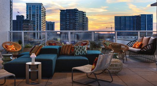 Patio with deep teal couches, rope wrapped chairs and colorful pillows with a city view