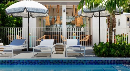 view of pool loungers with white umbrellas looking in to modern covered outdoor bar area